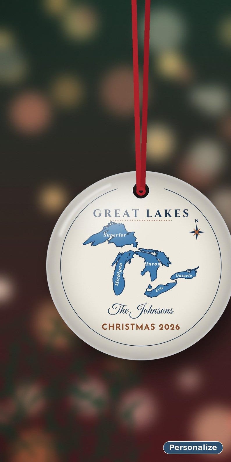 May include: A round white ceramic ornament hanging from a red ribbon. The design features a blue map of the Great Lakes labelled Superior, Michigan, Huron, Erie, and Ontario. Text reads GREAT LAKES, The Johnsons, and CHRISTMAS 2026.