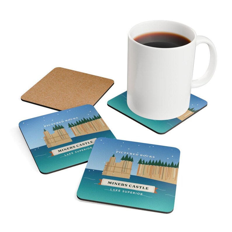 K&ouml;nnte beinhalten: Ein wei&szlig;er Keramikbecher mit schwarzem Kaffee steht auf einem quadratischen Untersetzer mit einer Grafik von Miners Castle an den Pictured Rocks am Lake Superior. Zwei weitere quadratische Untersetzer mit gleichem Motiv und ein Korkuntersetzer liegen bei.
