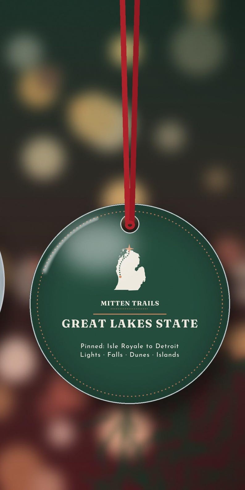 May include: A round, dark green ornament hanging from a red ribbon. The centre features a white map of Michigan with a star, the text MITTEN TRAILS, GREAT LAKES STATE, and Pinned: Isle Royale to Detroit Lights &middot; Falls &middot; Dunes &middot; Islands.