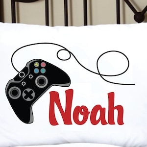 May include: White pillowcase with a black video game controller and a red embroidered name "Noah".