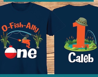 May include: A blue short-sleeved t-shirt with a fishing-themed design. The front of the shirt says "O-Fish-Ally one" with a cartoon fish and fishing rod. The back of the shirt has a large orange number one with a fishing hat and the name "Caleb".