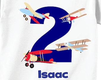 May include: White t-shirt with a blue number 2 and three red and blue airplanes. The name "Isaac" is printed below the number.