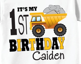 May include: White t-shirt with a yellow dump truck and the text "It's My 1st Birthday Caiden" on the front. The back of the shirt has a black and yellow striped number 1 with a smaller yellow dump truck and the name "Caiden".