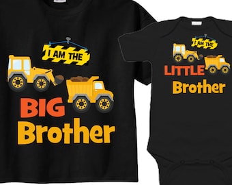 Op de afbeelding: Zwarte t-shirt en romper set met afbeeldingen van bouwmachines. Het t-shirt leest "BIG Brother" en de romper zegt "LITTLE Brother". Beide hebben gele bouwmachines en de tekst "I AM THE".