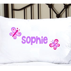 May include: White pillowcase with the name "Sophie" embroidered in purple with two pink butterflies on either side.