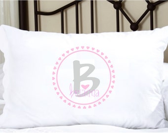 May include: White pillowcase with a pink and gray design. A gray letter "B" is centered, with the name "Brianna" in pink script below. The letter is inside a pink circle with pink hearts.