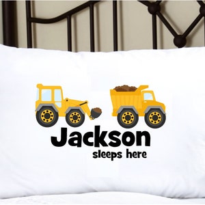 May include: White pillowcase with a yellow construction truck and excavator design. The text "Jackson sleeps here" is printed below the trucks.