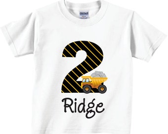 May include: White t-shirt with a black and yellow striped number 2, a yellow dump truck with gray rocks, and the name "Ridge" in black.