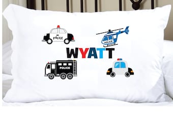 May include: White pillowcase with a black and white police car, a black police truck, a blue helicopter, and the name Wyatt in red, blue, and black letters.