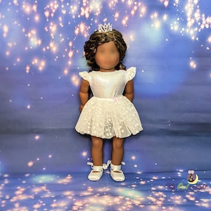 May include: A white tulle dress with a glittery bodice and a floral pattern. The dress is worn by a doll with brown hair and a silver crown. The doll is standing on a blue background with white stars.