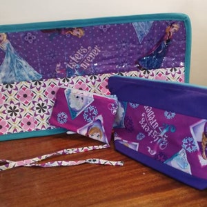 Puede incluir: Dos bolsas de tela de color morado y turquesa con temática de Frozen. La bolsa más grande tiene una cremallera y una correa. La bolsa más pequeña tiene una cremallera y un diseño de copo de nieve. Ambas bolsas tienen el texto "Sisters are forever" impreso en ellas.
