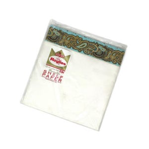 May include: A package of Roylies decorative shelf paper in a clear plastic wrapper. The paper features a white surface with a decorative border in shades of blue, brown, and gold. The label reads 15 ft. long for 29c Shelf Paper.