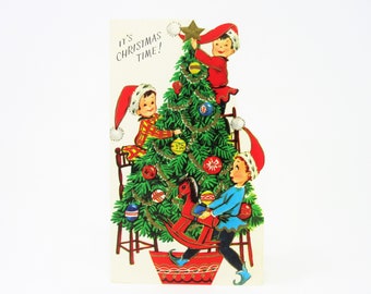 Vintage Unused Christmas Greeting Card Features Three Elves Two Decorate a Festive Tree and Wear Santa Hats and One Carries a Rocking Horse