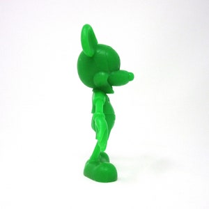 May include: A green plastic figurine of Mickey Mouse standing with his right arm raised and his left arm at his side. The figurine is facing to the right.