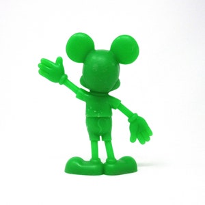 May include: A green plastic figurine of Mickey Mouse with his right arm raised in a wave. He is wearing shorts and has a friendly expression.