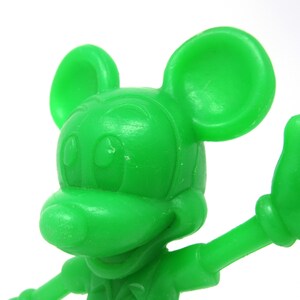 May include: A bright green plastic figurine of Mickey Mouse with large ears, a wide smile, and one arm outstretched.
