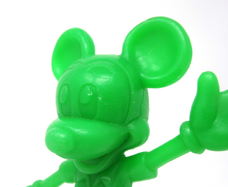 May include: A bright green plastic figurine of Mickey Mouse with large ears, a wide smile, and one arm outstretched.