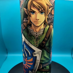 May include: A stainless steel tumbler with a green, blue, and orange image of Link from the Legend of Zelda video game series. The image shows Link wearing his signature green tunic and holding his Master Sword.