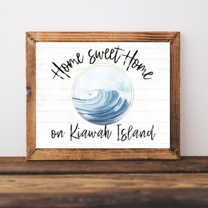 May include: A white wooden sign with the text "Home Sweet Home on Kiawah Island" in black cursive font. A blue watercolor wave is in a circle with a gold outline.