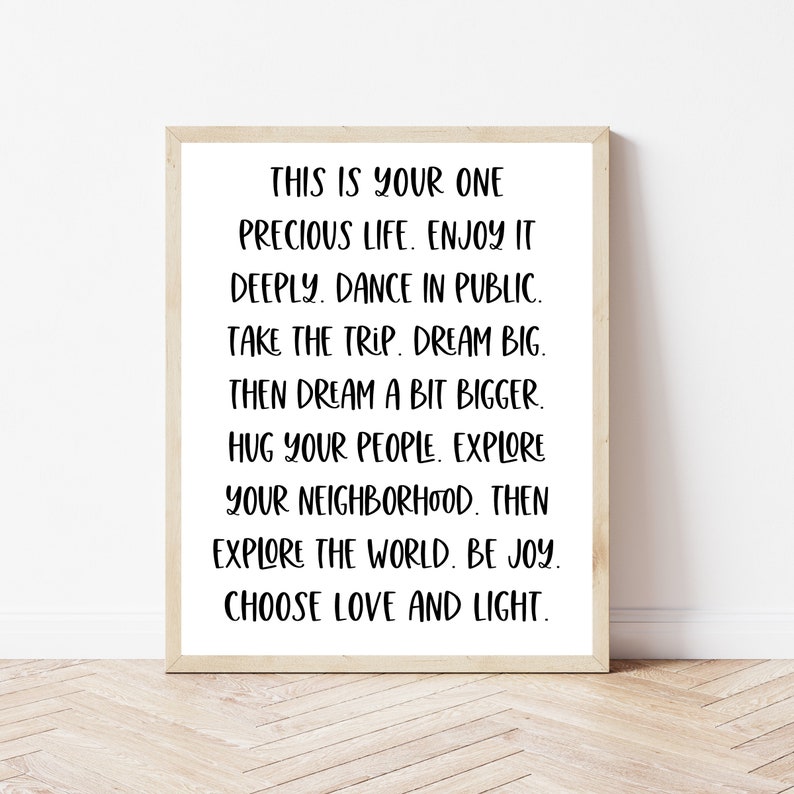May include: A framed print with a white background and black text that reads: "This is your one precious life. Enjoy it deeply. Dance in public. Take the trip. Dream big. Then dream a bit bigger. Hug your people. Explore your neighborhood. Then explore the world. Be joy. Choose love and light."