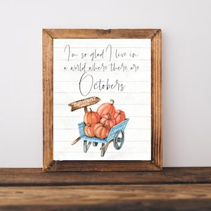 Peut inclure: Une pancarte blanche avec le texte "I'm so glad I live in a world where there are Octobers" en écriture cursive noire. Un chariot bleu avec une pancarte en bois qui dit "Pumpkin Patch" est rempli de citrouilles orange.