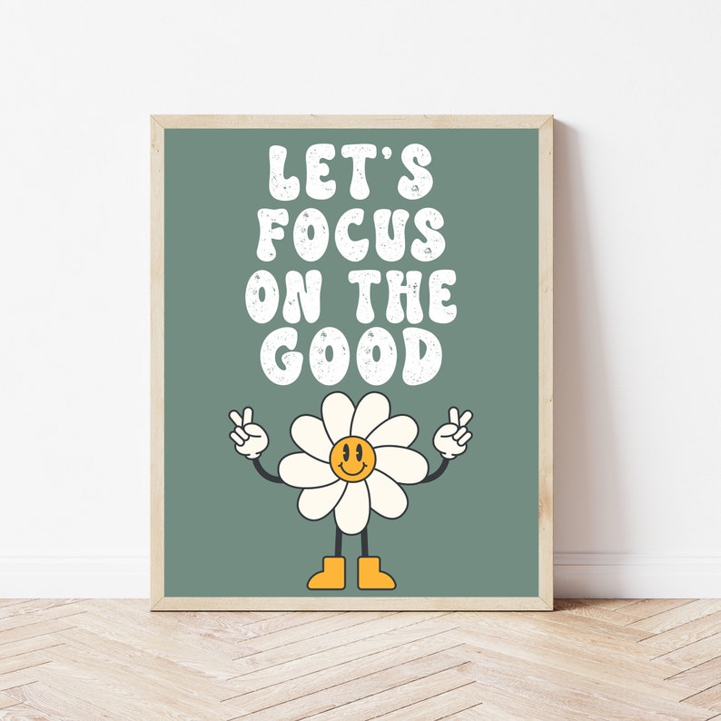 以下が含まれることがあります： 緑色のポスターに、レトロなスタイルの白い文字で「Let's Focus on the Good」と書かれています。テキストの下には、笑顔の顔とピースサインをした漫画のひまわりがあります。