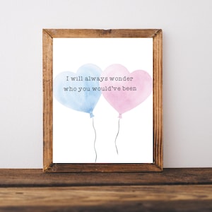 May include: A framed print with a white background and the text "I will always wonder who you would've been". Two watercolour heart-shaped balloons, one blue and one pink, are floating above the text.