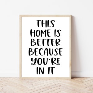 May include: A framed print with a white background and black text that reads "This home is better because you're in it".