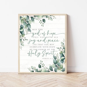 Puede incluir: Un diseño de arte de pared imprimible con un fondo de madera blanca y hojas de eucalipto verdes. El texto dice "Que el Dios de esperanza te llene de toda alegría y paz para que puedas rebosar de esperanza por el poder del Espíritu Santo Romanos 15:13".