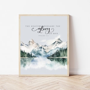 May include: A watercolor painting of a mountain range with a lake in the foreground. The sky is a light blue and the mountains are a light gray with white snow on the peaks. The lake is a light blue and there are trees on the shore. The text "THE HEAVENS DECLARE THE GLORY OF GOD PSALM 19:1" is written in black at the top of the image.