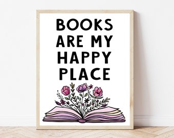May include: A white framed print with black text that reads "BOOKS ARE MY HAPPY PLACE". The text is centered on the print. Below the text is a pink and purple open book with flowers growing out of it.