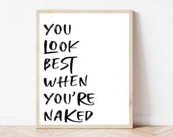 May include: A framed print with the text "YOU LOOK BEST WHEN YOU'RE NAKED" in black script on a white background. The frame is a light wood color, and the print is displayed on a wooden floor.