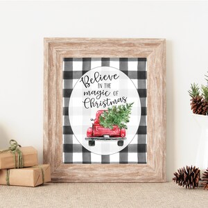 Puede incluir: Un cartel de Navidad imprimible con un camión rojo que lleva un árbol de Navidad. El camión está en un círculo blanco con un fondo de cuadros de búfalo blanco y negro. El texto en el cartel dice "Cree en la magia de la Navidad".