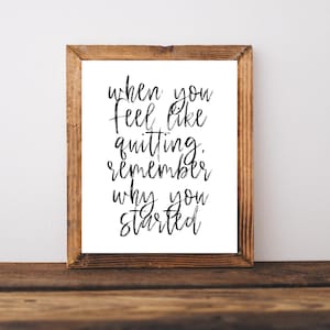 May include: A framed print featuring the quote "when you feel like quitting, remember why you started" in black script on a white background. The frame is made of rustic, light brown wood. The print is displayed on a wooden surface.