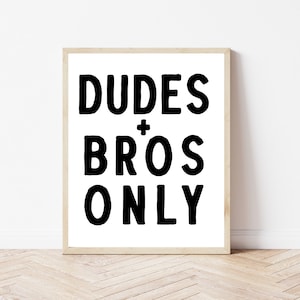 Könnte beinhalten: Ein schwarz-weißer gerahmter Druck mit dem Text "DUDES + BROS ONLY" in einer fetten, handgeschriebenen Schrift.