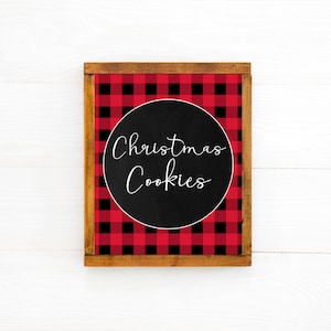 May include: A wooden sign with a red and black buffalo plaid pattern. The sign has a black circle in the center with the text "Christmas Cookies" written in white.