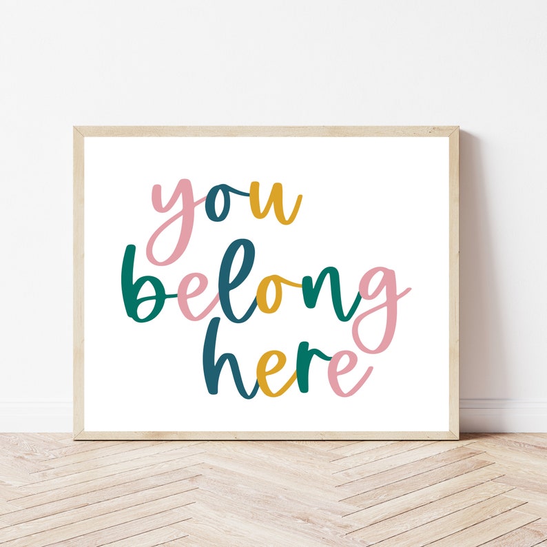 K&ouml;nnte beinhalten: Ein gerahmter Druck mit dem Text "you belong here" in einer bunten, handgeschriebenen Schrift. Die W&ouml;rter sind in den Farben Rosa, T&uuml;rkis und Gold gehalten.