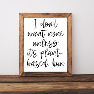 May include: A framed print with a white background and black text that reads "I don't want none unless it's plant-based, hun". The frame is brown wood.