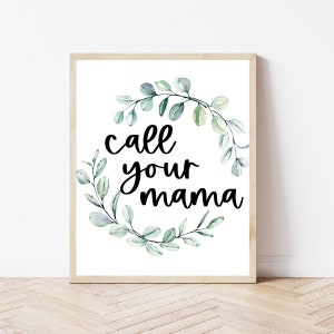 May include: A white framed print with a green watercolor wreath and the text "call your mama" in black.