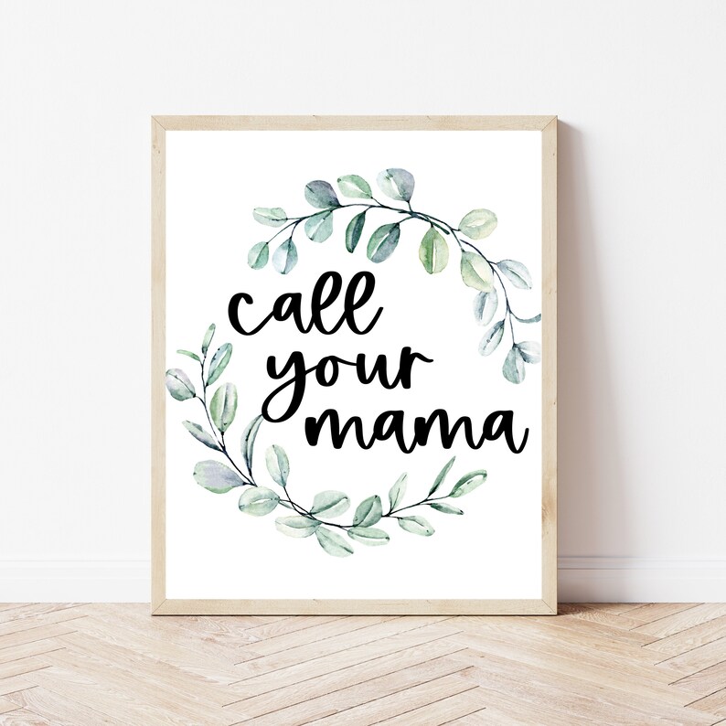 May include: A white framed print with a green watercolor wreath and the text "call your mama" in black.