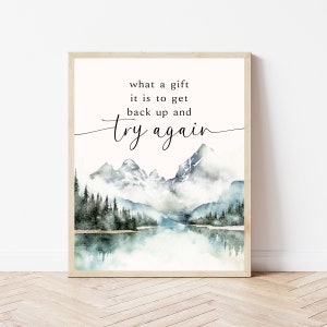 Könnte beinhalten: Ein Aquarelldruck mit einem Zitat, das lautet: "Was für ein Geschenk es ist, wieder aufzustehen und es erneut zu versuchen". Das Bild zeigt eine Bergkette mit einem See im Vordergrund.