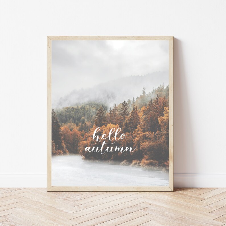 Op de afbeelding: Een ingelijste print met een foto van een mistige bos sc&egrave;ne met een rivier op de voorgrond. De tekst "hello autumn" is in witte cursieve letters op de afbeelding geschreven.