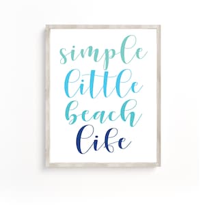 May include: A white framed print with the text "simple little beach life" in blue and teal gradient lettering.