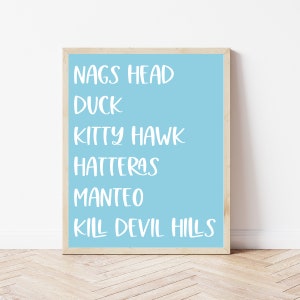 Puede incluir: Una impresión enmarcada azul claro con los nombres de las ciudades de Outer Banks en texto blanco: Nags Head, Duck, Kitty Hawk, Hatteras, Manteo, Kill Devil Hills.