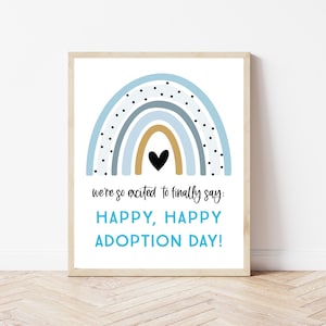 Könnte beinhalten: Ein druckbares Schild mit einem blauen und goldenen Regenbogen mit schwarzen Punkten und einem schwarzen Herzen in der Mitte. Der Text lautet "we're so excited to finally say: HAPPY, HAPPY ADOPTION DAY!"