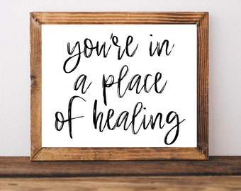 May include: A framed print with the text "you're in a place of healing" in black cursive script on a white background.