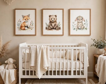 May include: Three framed wall art prints featuring watercolor illustrations of a fox, a bear, and a rabbit, each surrounded by botanical elements. The prints are displayed in light wood frames above a white crib with a cream-colored blanket.