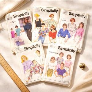 May include: A collection of vintage Simplicity sewing patterns. The patterns feature illustrations of women's clothing designs, including blouses and tops. The patterns are in various sizes and styles, with the Simplicity logo prominently displayed.