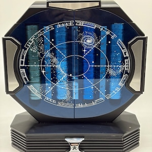 May include: A black octagonal display case with a blue glass front featuring a white star map and grid design. The interior contains four vertical stacks of blue circular tokens. A silver Starfleet insignia is centered on the base drawer handle.