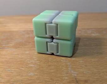 May include: A mint green and light grey plastic infinity cube fidget toy composed of eight small connected blocks that can be folded and manipulated into various shapes, featuring a smooth matte finish on all visible surfaces.
